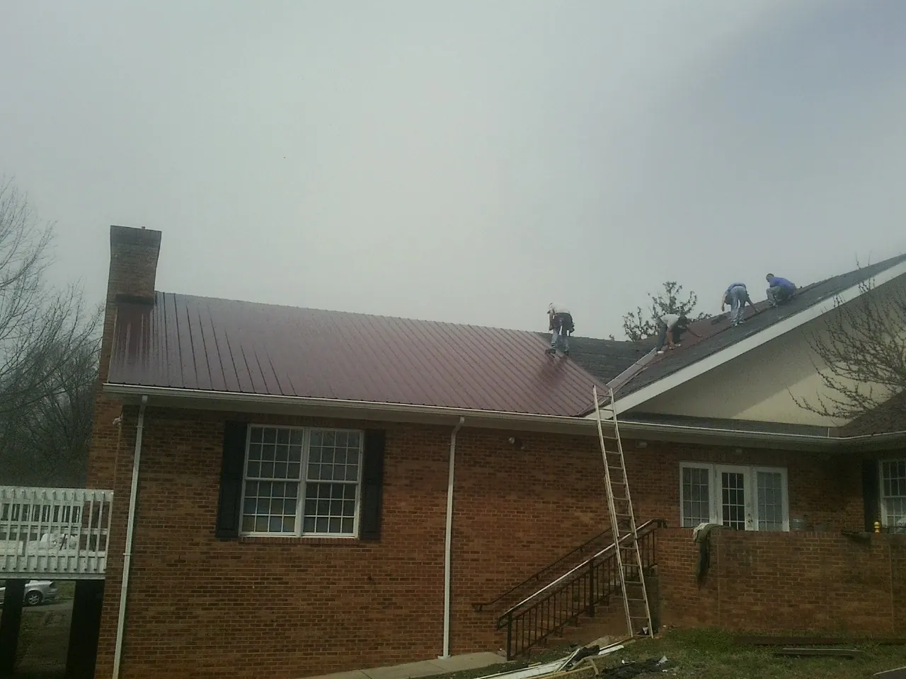 Crew setting red metal roofing panels on a brick home in Atwood