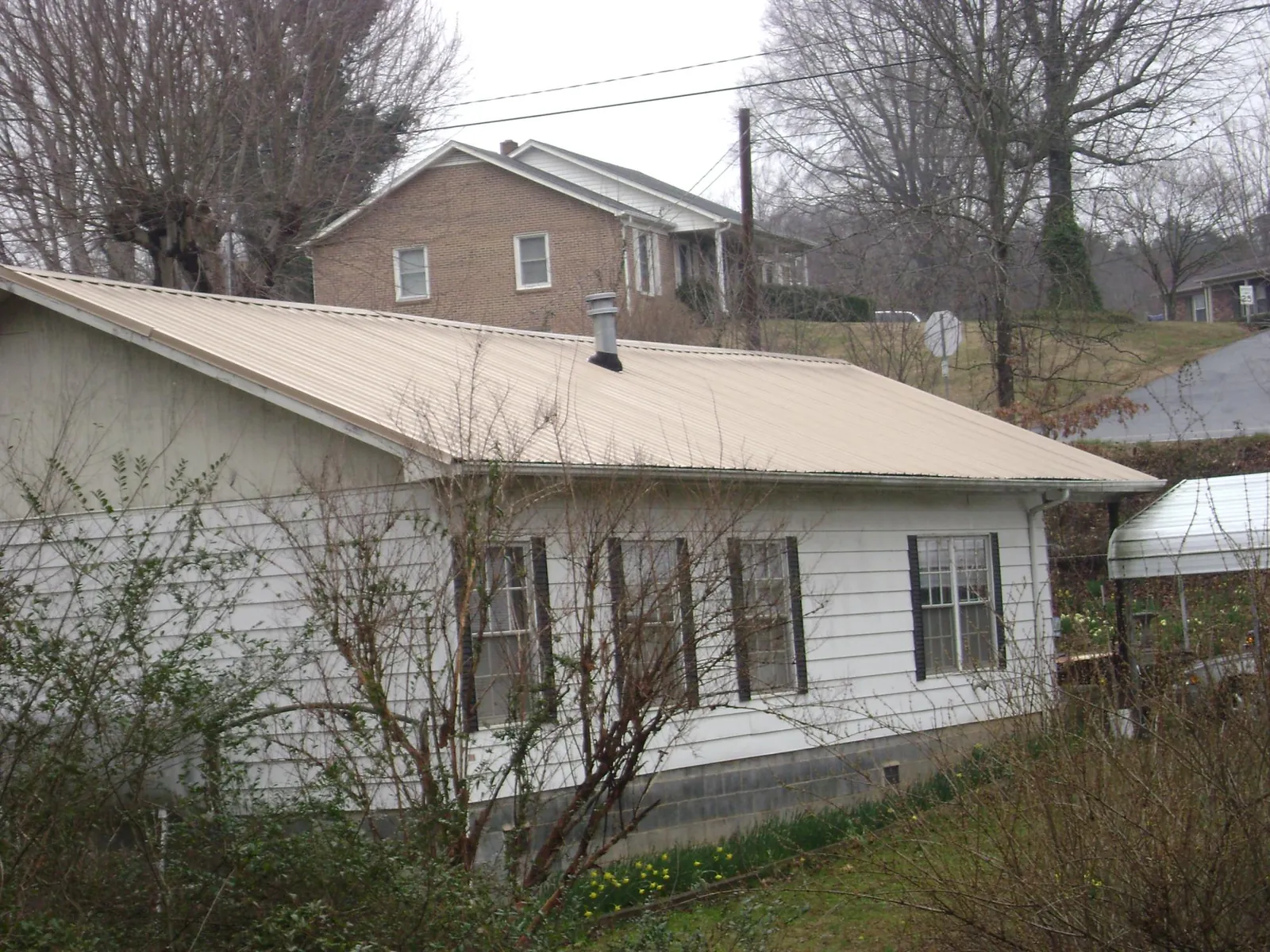 Tan metal roof on a white sided house set into a hillside — Commercial Roofing by Roofing Brothers in Atwood